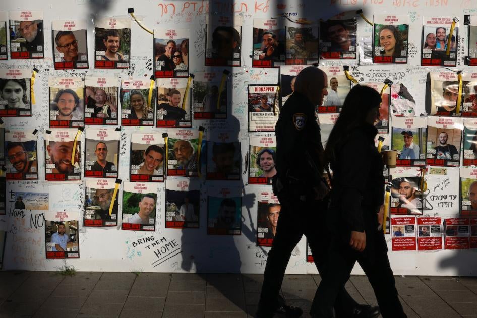 Un policier israélien et une femme marchaient devant un mur ou étaient collées des photos d’otages enlevés le 7 octobre 2023 par des combattants du Hamas et détenus à Gaza, dans une rue de Tel Aviv, le 17 décembre 2023.